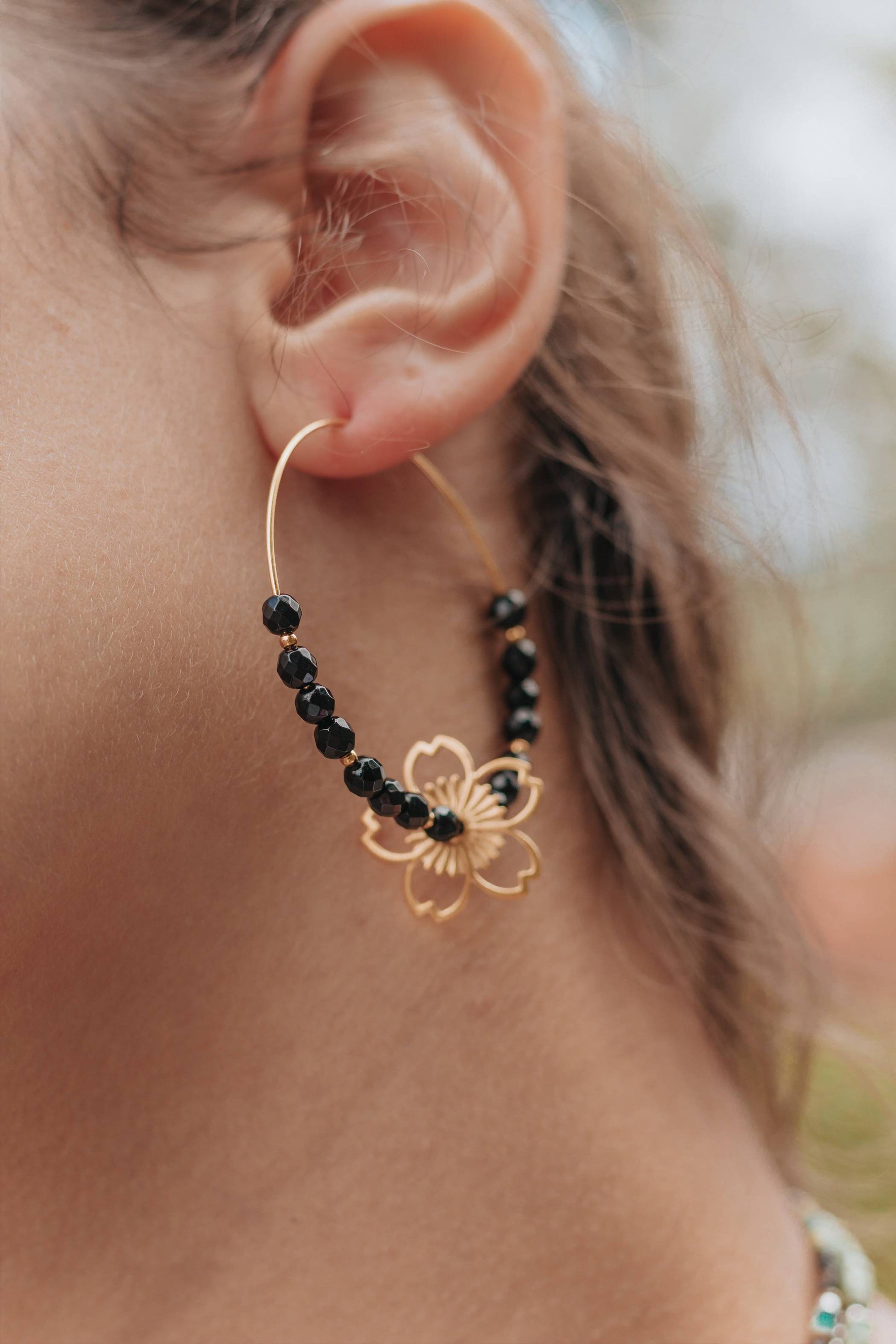 Sublimez votre look avec ces élégantes créoles dorées en argent 925, ornées de pierres d'onyx naturelles et d'une délicate fleur estampée.